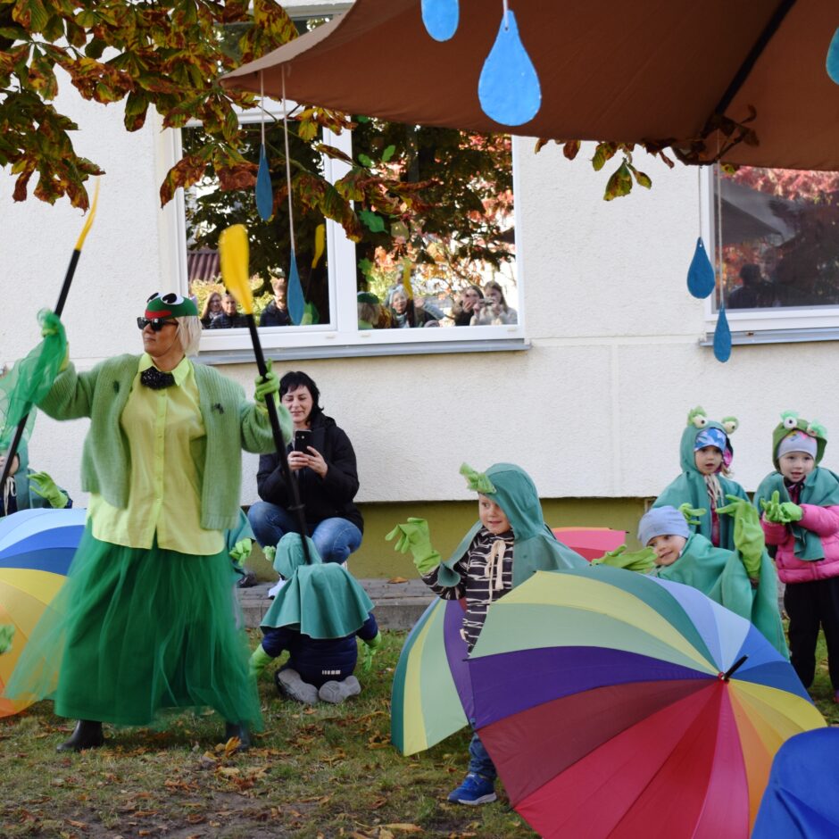 Bērni tērpušies kostīmos un dejo bērnudārza pagalmā.