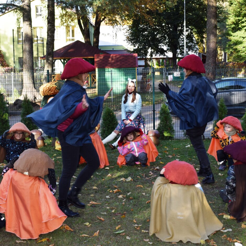 Bērni tērpušies kostīmos un dejo bērnudārza pagalmā.