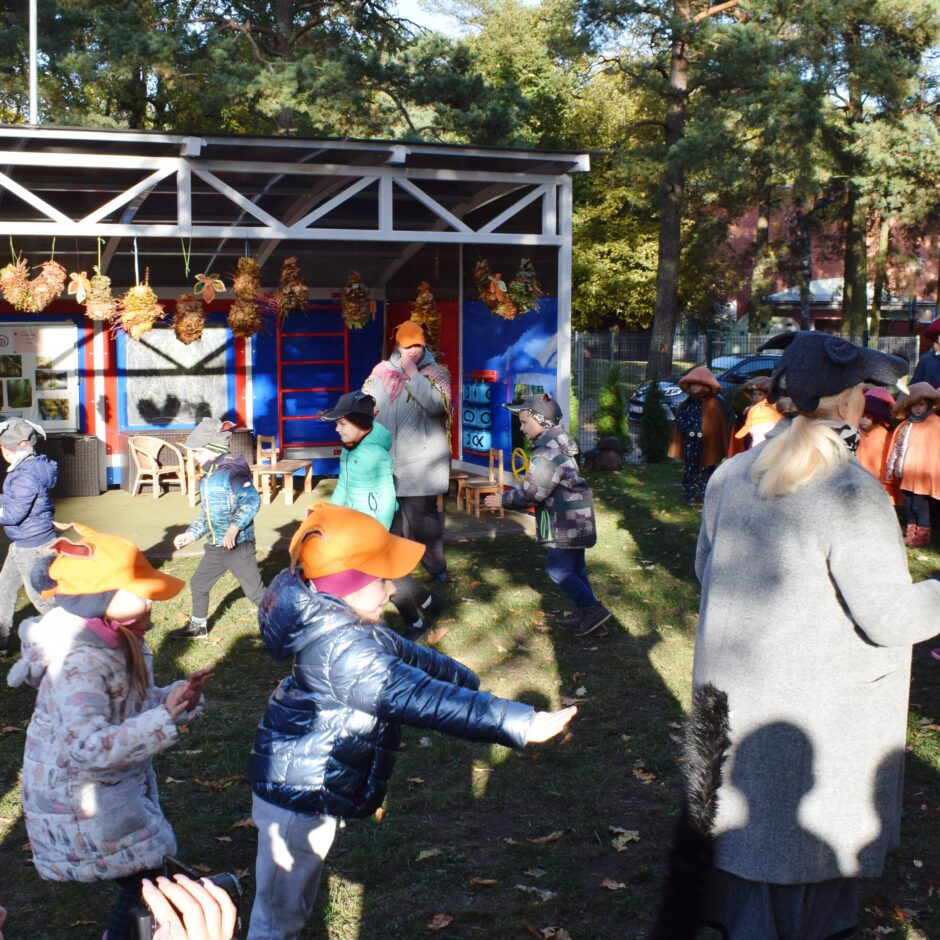 Bērni tērpušies kostīmos un dejo bērnudārza pagalmā.